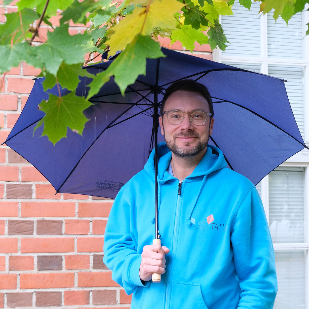 Kuvassa Petri Partanen VAUHTI! -toiminnan suunnittelija pitelee sateenvarjoa ja hymyilee