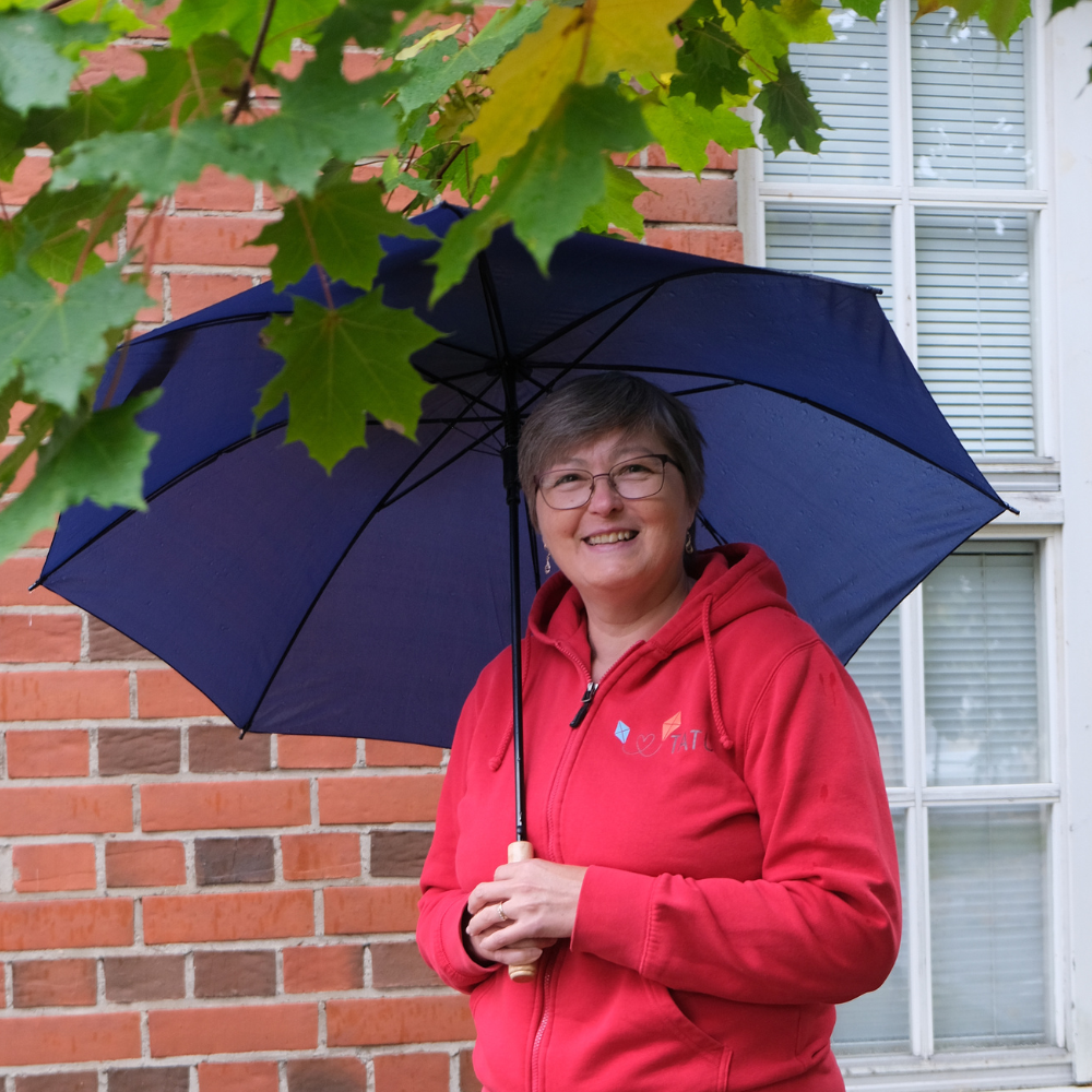 Kuvassa Anu Karjalainen TATUn toimistosihteeri pitelee sateenvarjoa ja hymyilee