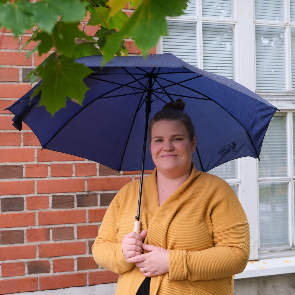 Kuvassa Emma Lappi TATUn kurssisuunnittelija ja hankesuunnittelija pitelee sateenvarjoa ja hymyilee
