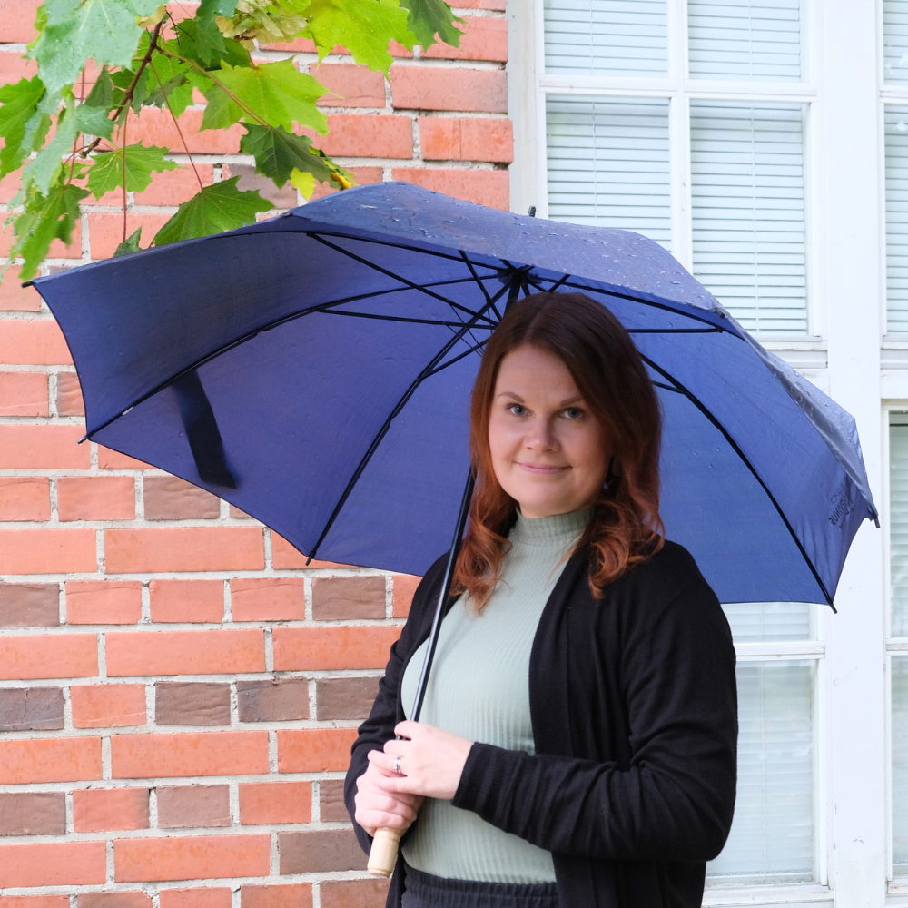Kuvassa Eija Saario TATUn viestintäsuunnittelija pitelee sateenvarjoa ja hymyilee