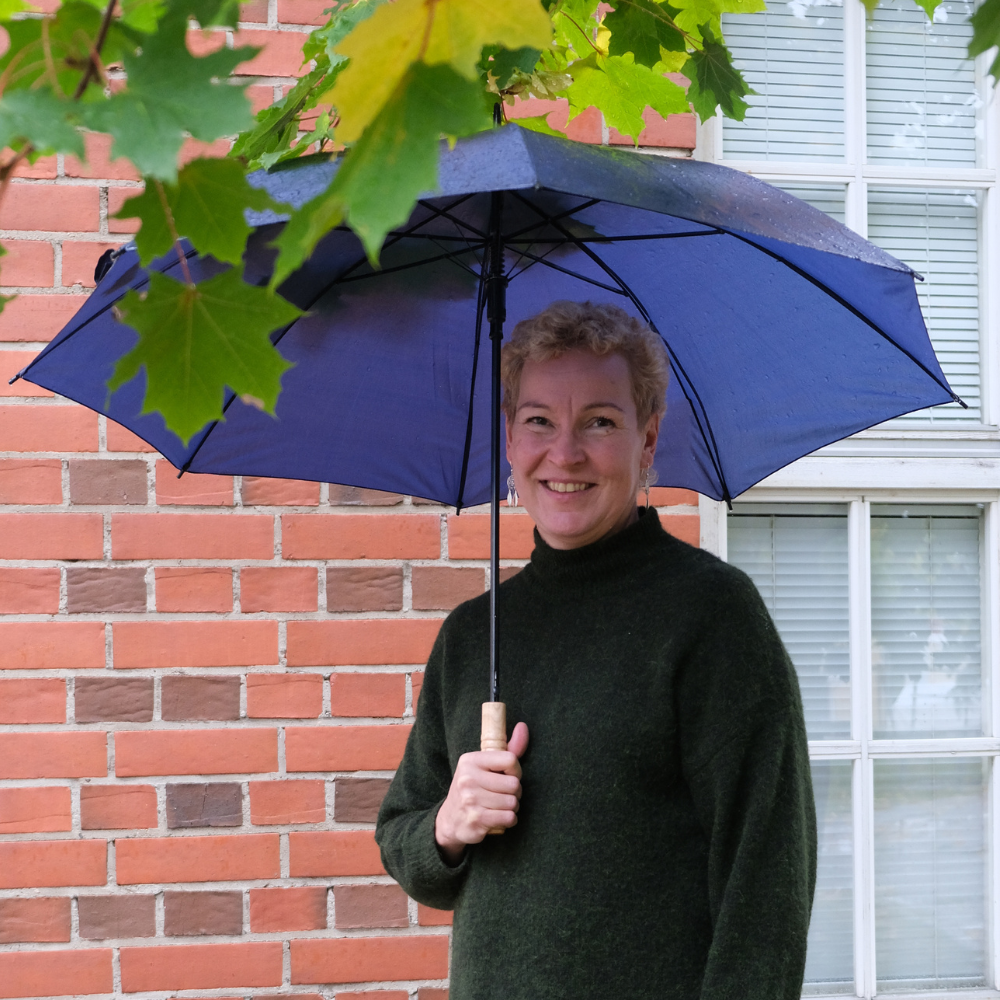 Kuvassa Tiina Männistö järjestösuunnittelija pitelee sateenvarjoa ja hymyilee