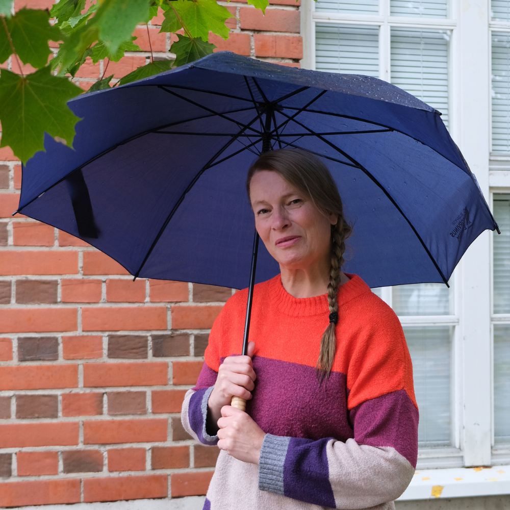Kuvassa Anu Hämäläinen TATUn järjestösuunnittelija ja aluekoordinaattori pitelee sateenvarjoa ja hymyilee