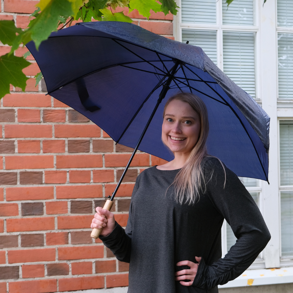 Kuvassa Tessa Ollila VAUHTI! -toiminnan suunnittelija pitelee sateenvarjoa ja hymyilee.