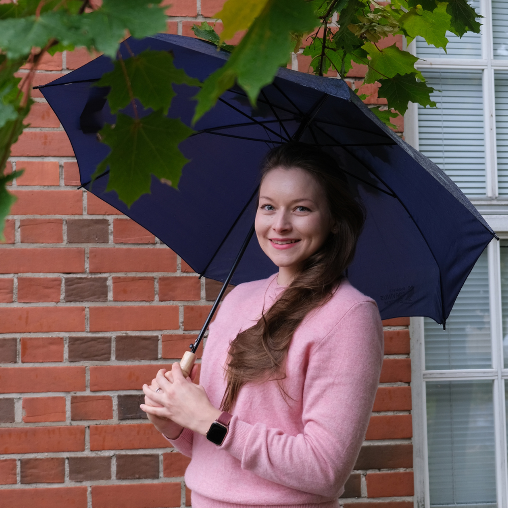Kuvassa Katja Ihalainen VAUHTI! -toiminnan suunnittelija pitelee sateenvarjoa ja hymyilee.